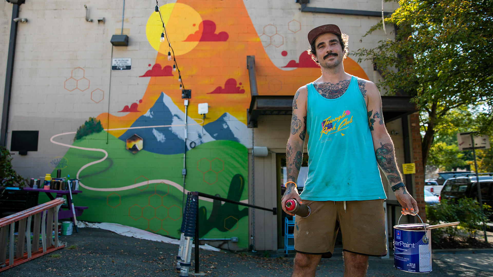 Artist The Night Owl poses in front of his CATAN themed mural
